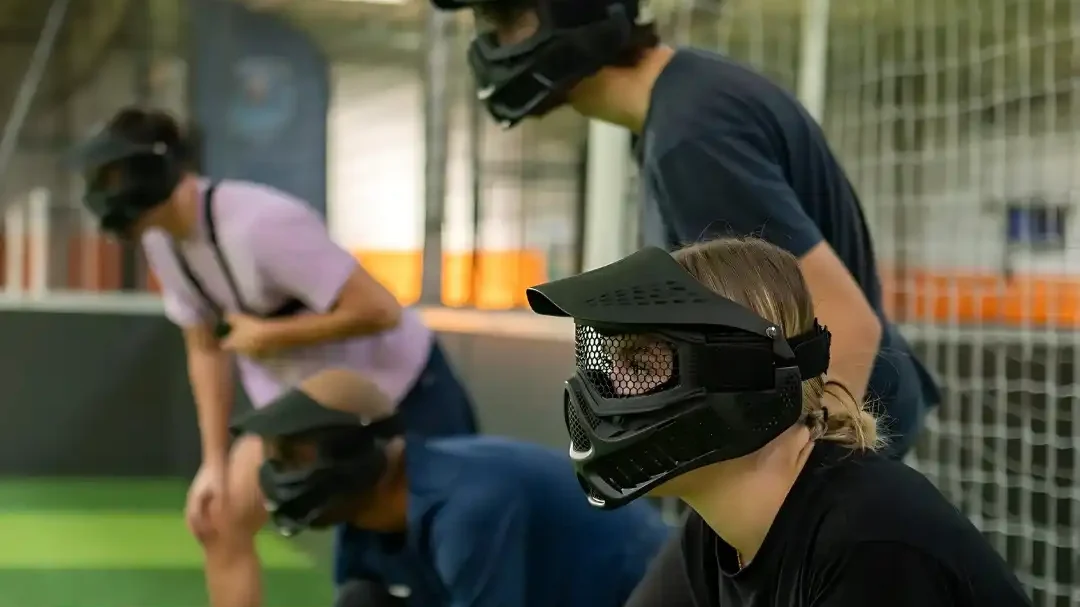 Des participants portant des masques écoutent en bordure d’un terrain intérieur